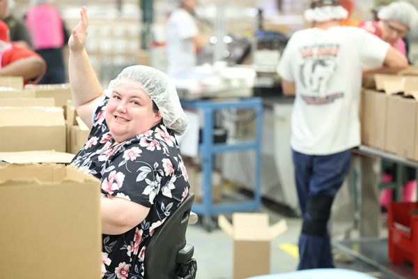 woman smiling and waving as she works in production plant