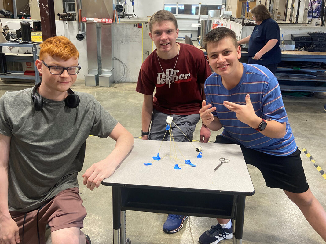 Three high school boys standing behind the tower they build from spaghetti at BCI Summer Camp