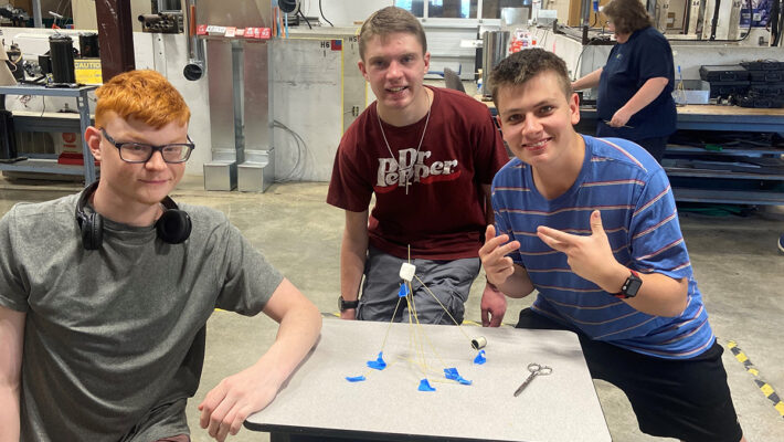 Three high school boys standing behind the tower they build from spaghetti at BCI Summer Camp