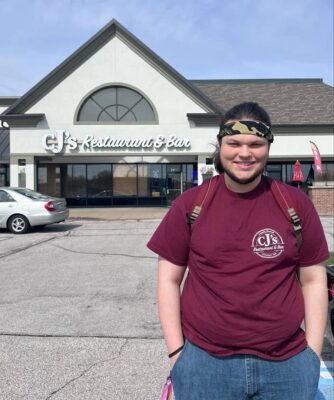 Young man standing in front of restaurant where he works