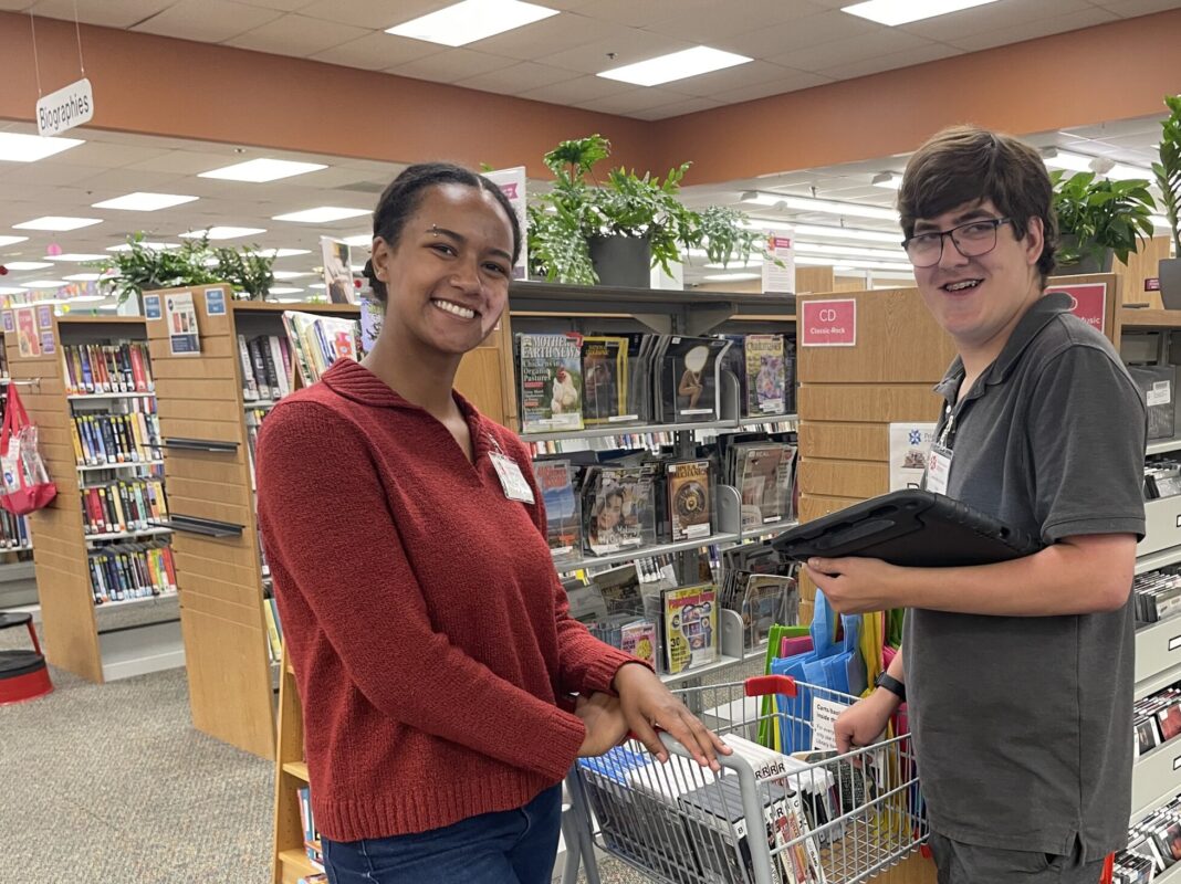 High school student with disabilities working in a library with his job coach in BCI's summer work program