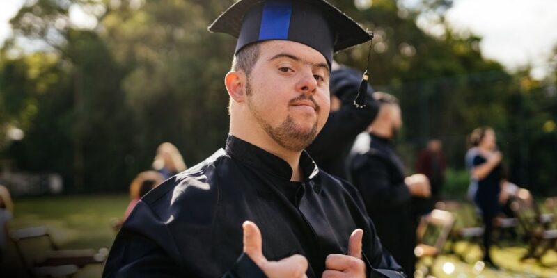 A high school graduate with Autism giving thumbs up in his cap and gown