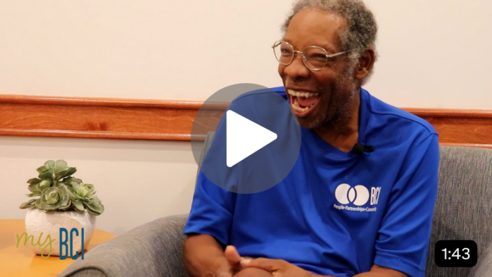 An older man in a blue BCI shirt smiling and launching